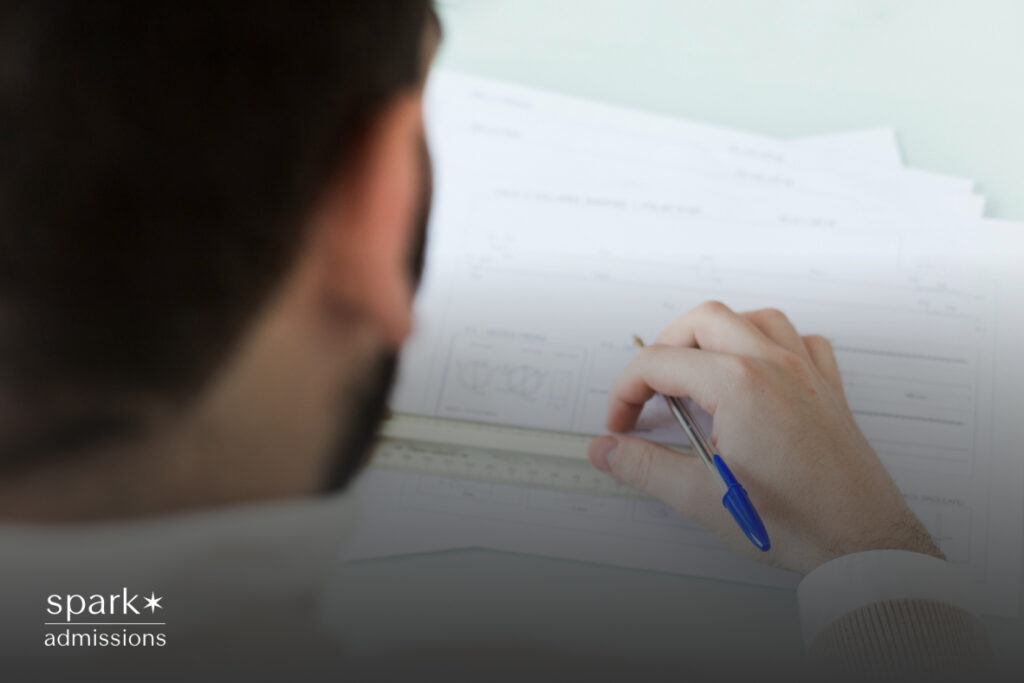 A person sitting at a desk, focused on taking an exam, with a pen in hand and papers spread out in front of them.