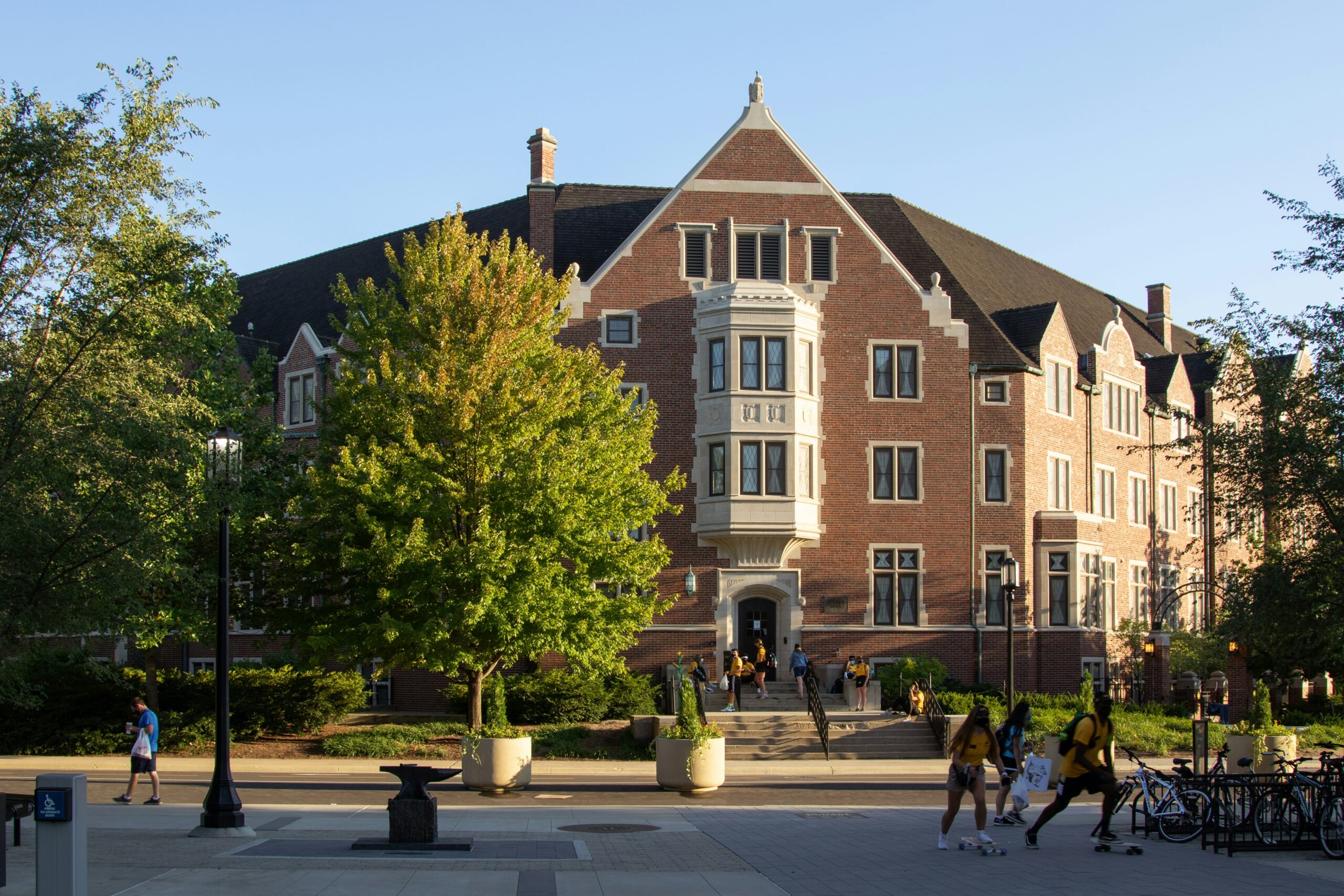 Historic red-brick academic building of Purdue University with students walking and skateboarding on a sunny day