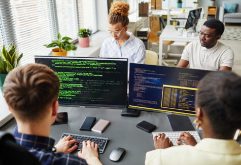 Group of software developers sitting at desk with computer monitors and working with codes of new software at office