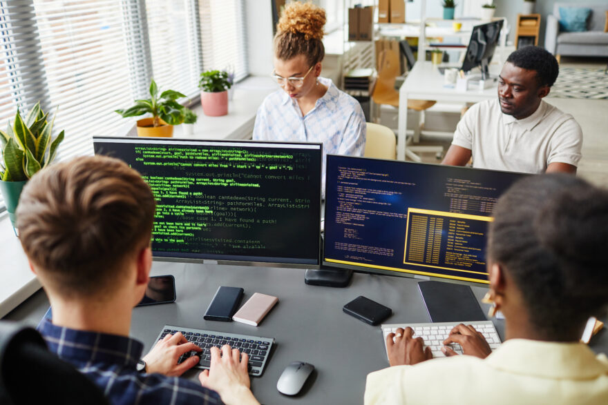 Group of software developers sitting at desk with computer monitors and working with codes of new software at office