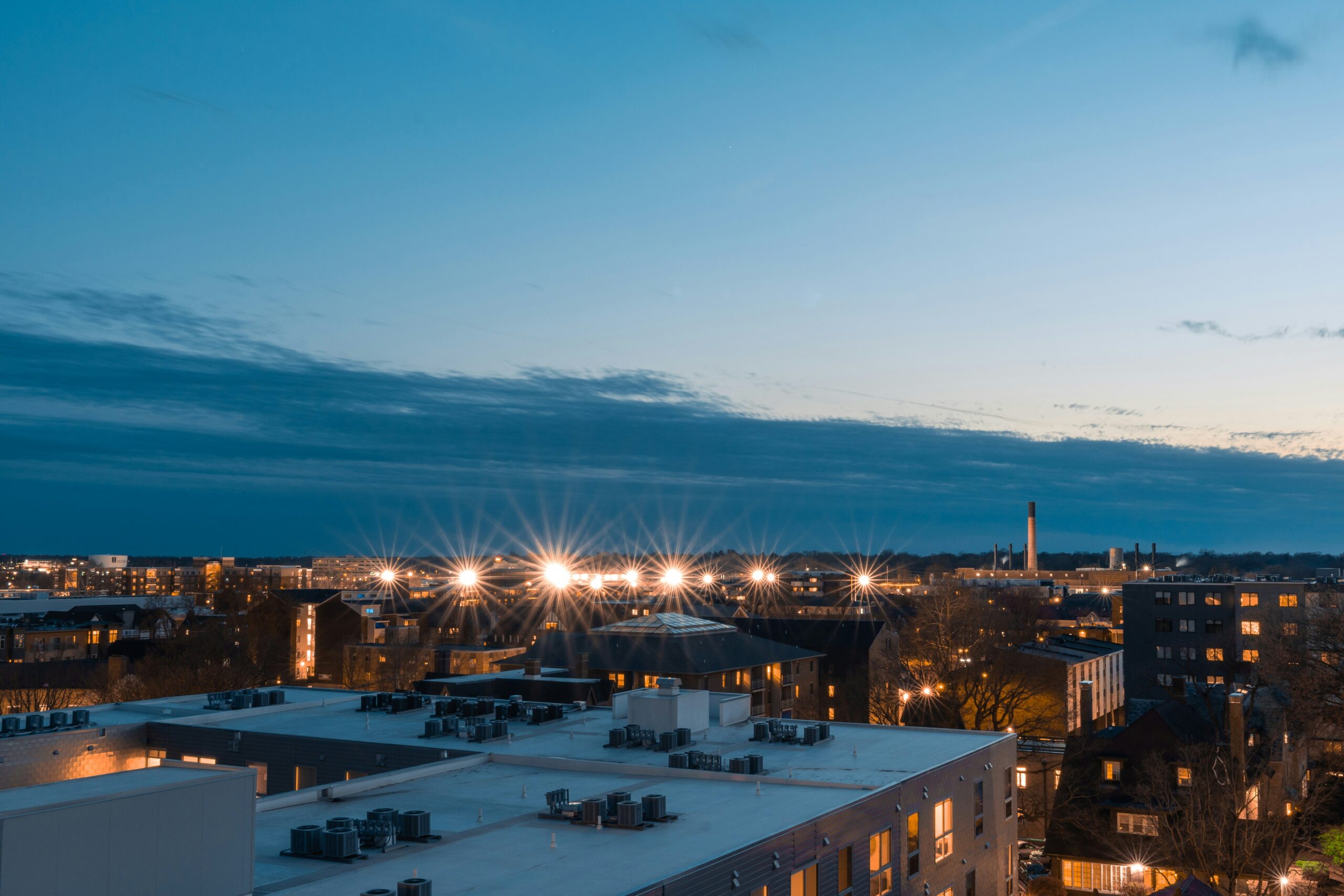 Cityscape at University of Illinois Urbana-Champaign campus with rooftops, lights, and distant buildings under a darkening sky