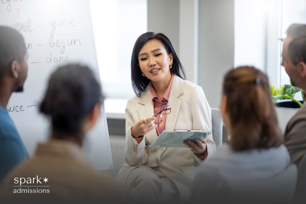 An Asian teacher engaged in discussion with a group of focused students in a classroom setting, pointing to a whiteboard with detailed notes, fostering an interactive and collaborative learning environment.