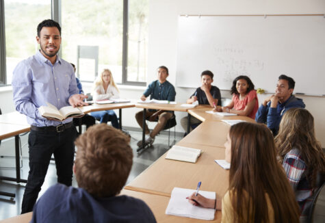 A group of students seated around a round table, with one person in the center leading a discussion about a business course.